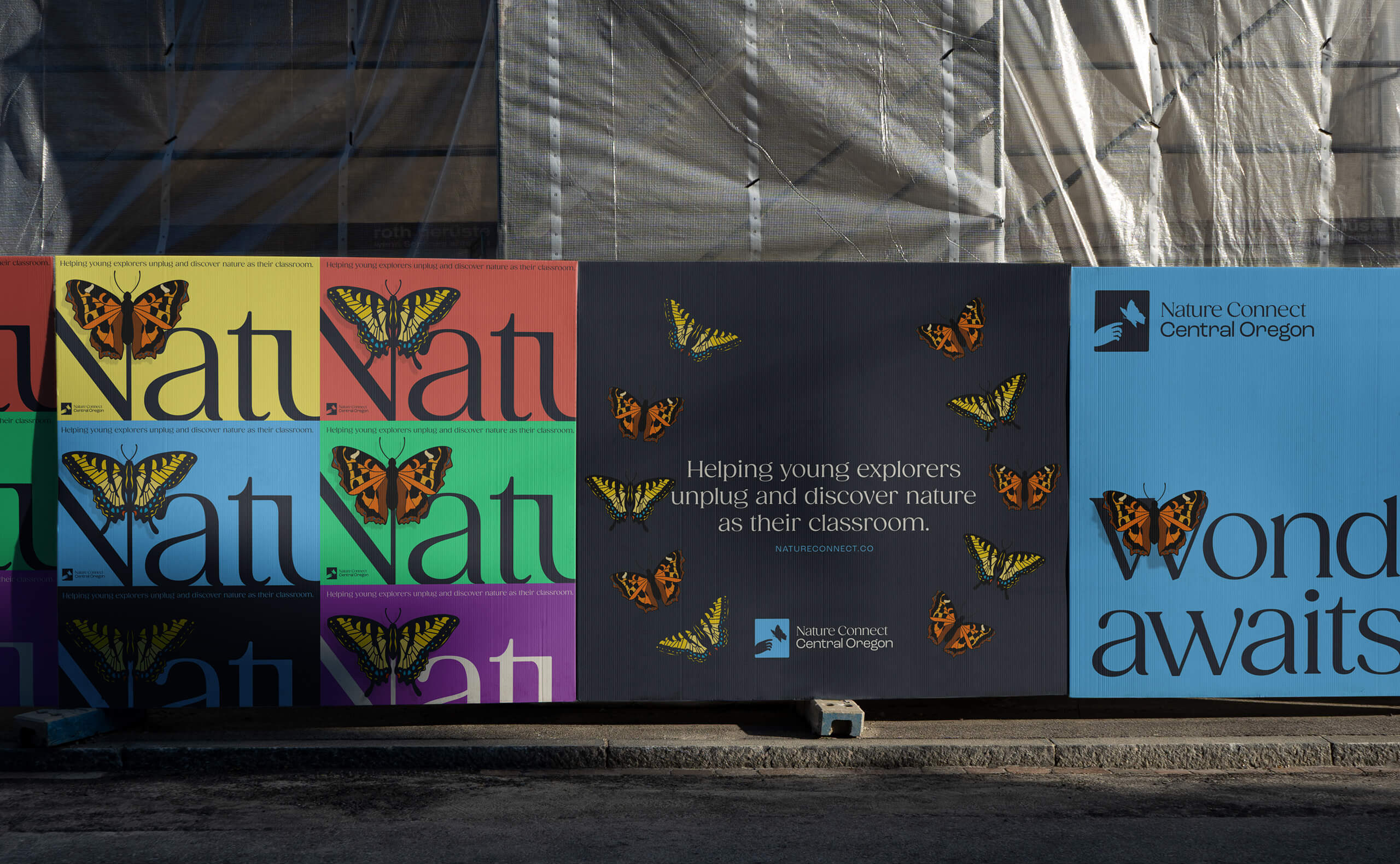 A large poster featuring bold color blocks, stylized butterflies, and text reading ‘Helping young explorers unplug and discover nature as their classroom.’